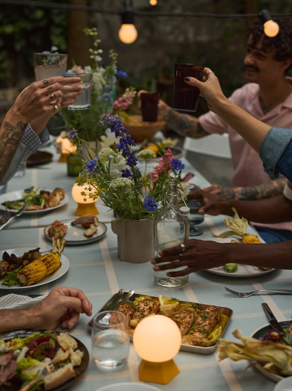 人们持有眼镜长桌子盘子的食物,鲜花和SOMMARLANKE LED台灯在一个聚会上。