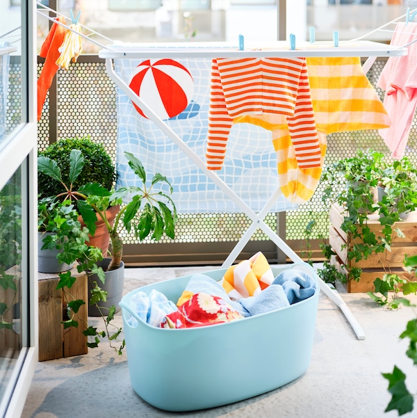 蓝色TORKIS福莱希洗衣篮装满衣服和MULIG干燥器在一个阳光明媚的阳台装饰着植物。