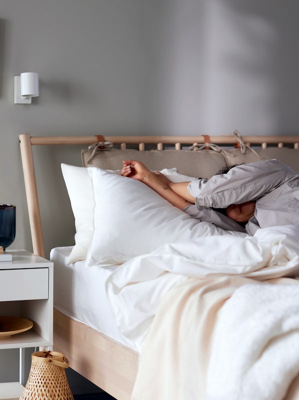 一个人在birch-frame睡衣躺在床上用白色ANGSLILJA床单,白色VIKHAMMER床头柜旁边。