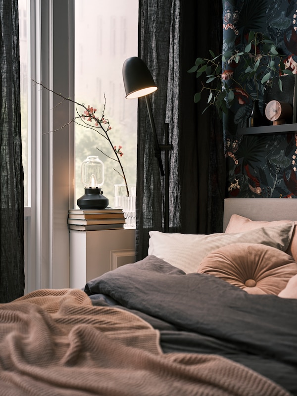 黑色的地板/ SKURUP台灯在床旁边,旁边一个窗口与深灰色DYTAG窗帘和TARNABY台灯。