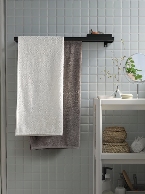 黑色SKOGSVIKEN的挂毛巾的横杆上挂着一个托盘,瓷砖墙用一个棕色毛巾和一条白毛巾。