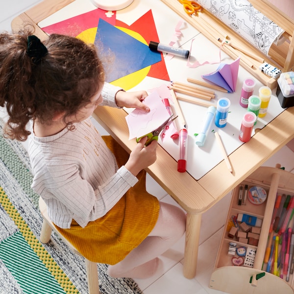 一个女孩坐在FLISAT儿童表FLISAT儿童凳子上手工制作和使用叶的颜色。