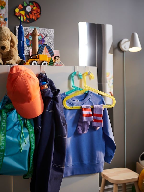 各种衣服儿童衣架和一个背包挂在LATTHET钩子和剪辑在一个白色的衣柜。