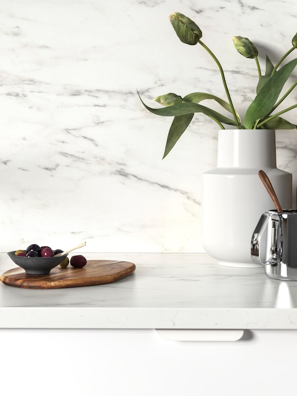 白色EKBACKEN桌面铺着大理石效果,橄榄木砧板,和一个白色的花瓶郁金香。