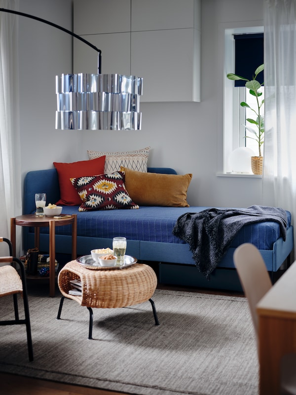 一个软垫床床头板框架角落,蓝色的床罩,彩色靠垫、脚凳与存储的零食。