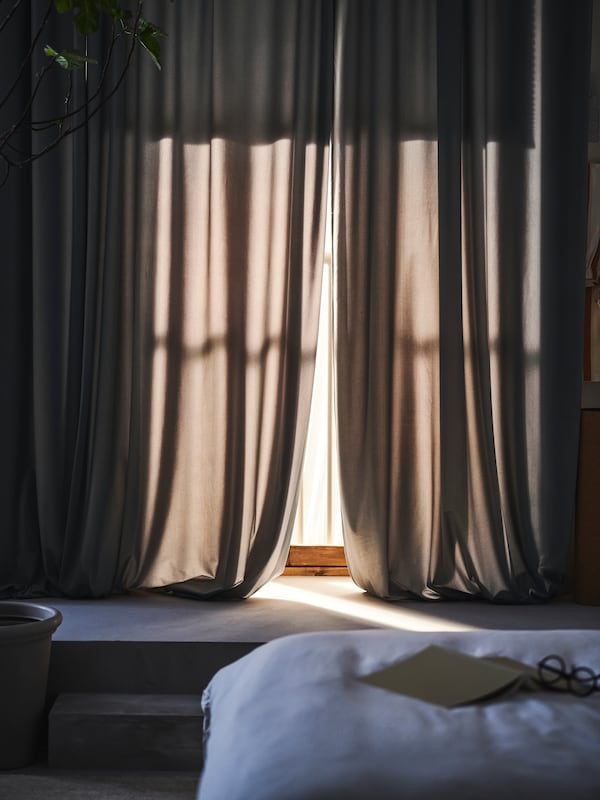 一双SANDSVINGEL卧室的窗帘挂在窗户附近SLATTUM软垫床SILVERTISTEL床单。