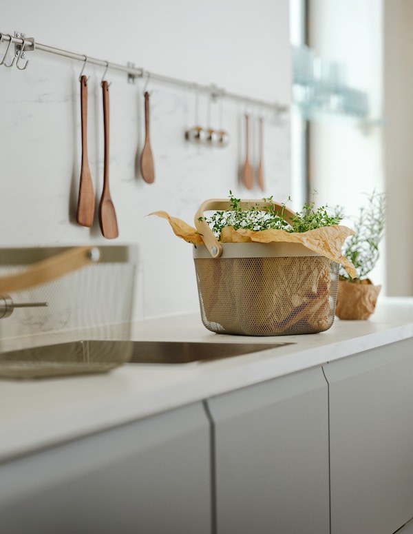 一个厨房和两个grey-beige RISATORP篮子放在水槽的两侧。一个复合纸和草药。