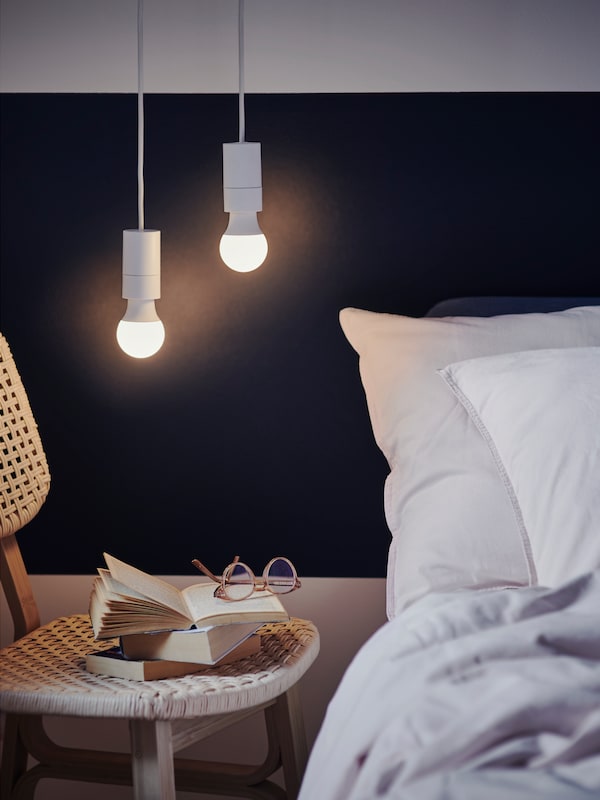 请来两verschiedene SOLHETTA LED-Leuchtmittel在SUNNEBY Lampenaufhangungen uber einem VOXLOV Stuhl neben einem Bett。