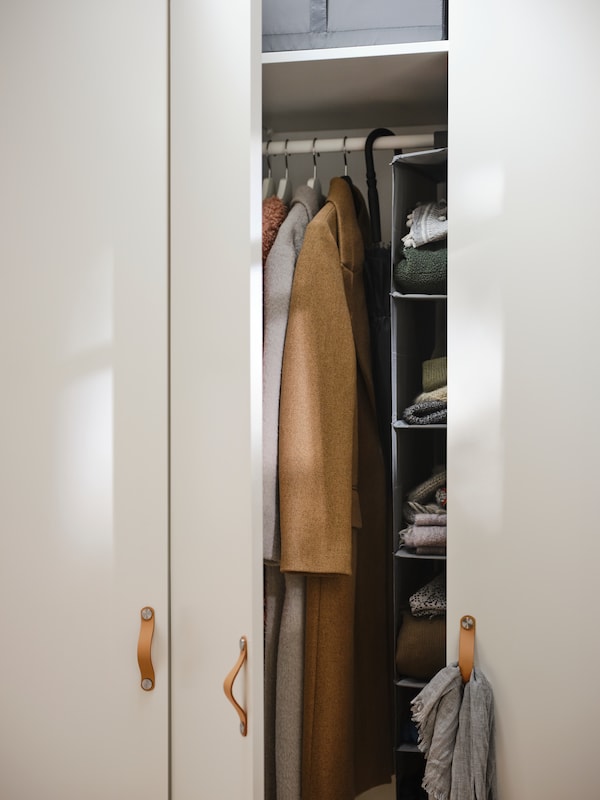 白色的罗马帝国/ FORSAND衣柜OSTERNAS皮革处理,一扇门打开显示外套挂在衣架上。