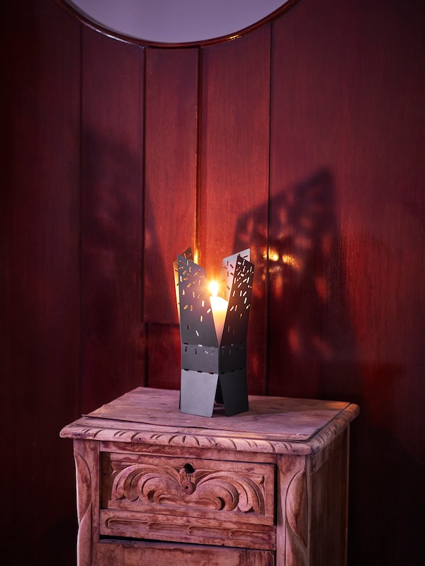 明信片grosse Kerze brennt在einem schwarzen OMSESIDIG Kerzenhalter在pulverbeschichtetem Stahl der auf einem holzernen Beistelltisch麻省理工学院Schnitzereien steht。