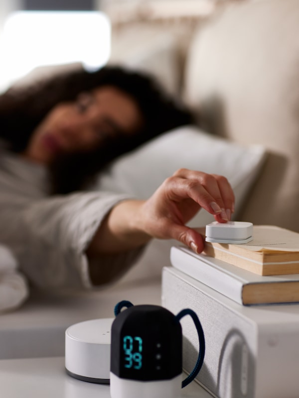 一个女人躺在床上推着TRADFRI无线调光器上的一些书和一个无线扬声器在白色的床头柜。