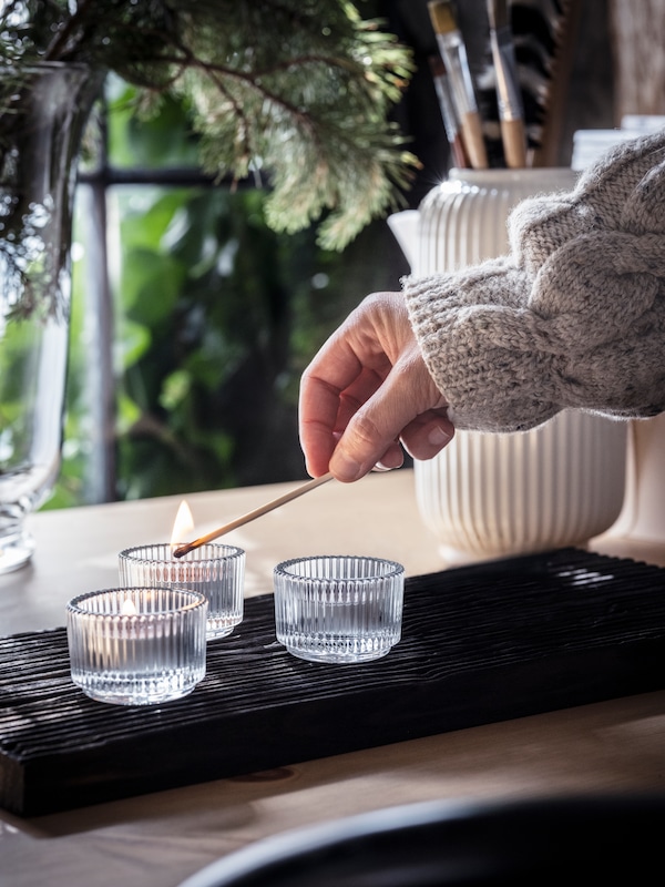 一只手照明三个ENSTAKA香味茶蜡用一根火柴放在桌上花瓶用松树枝。