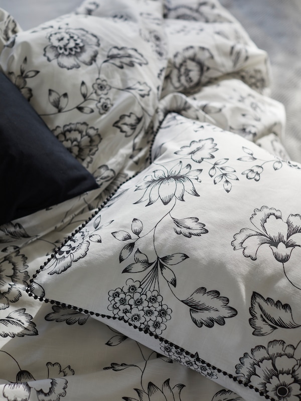 一个JUNGFRUNAVA被套和枕套白色/灰色花坐在床上,一个黑色的枕头也可见。