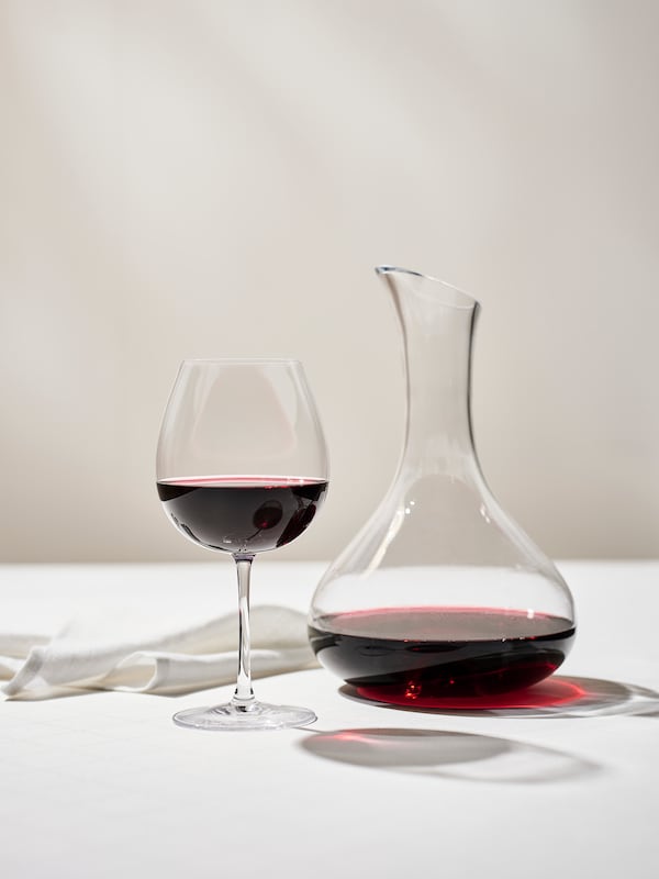 旁边一个半满STORSINT红酒杯,白布餐巾和STORSINT透明玻璃玻璃水瓶含有红酒。