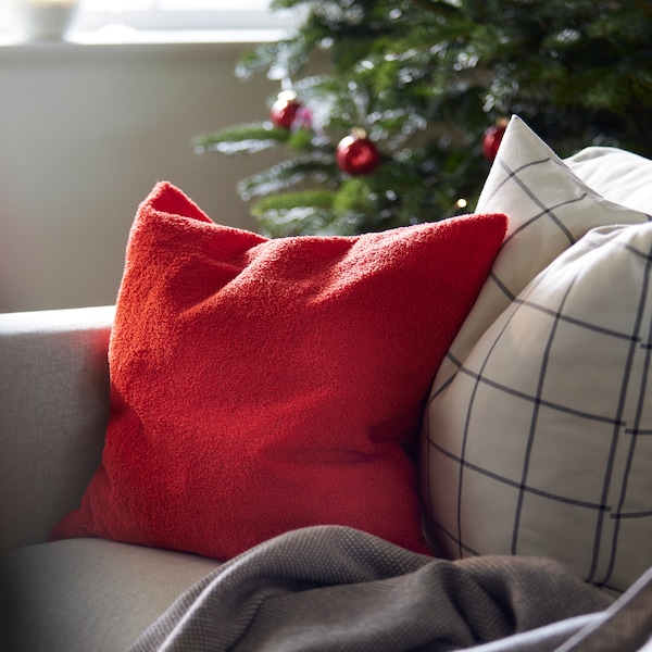 Punainen VINTERFINT-sarjan tyyny sekä ruudullinen SPIKKLUBBA-tyyny vaalealla sohvalla。