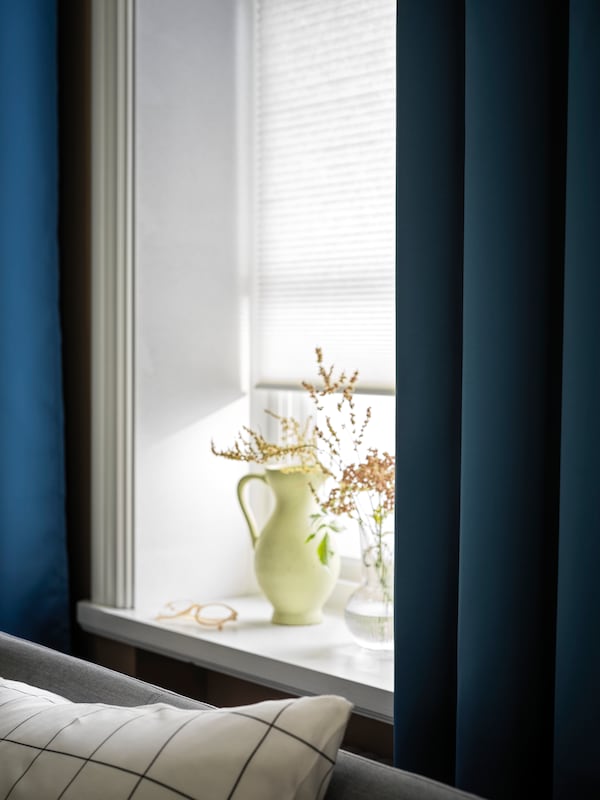 一张床,一个窗口在窗台上用鲜花,白色HOPPVALS细胞盲和蓝色HILLEBORG room-darkening窗帘。