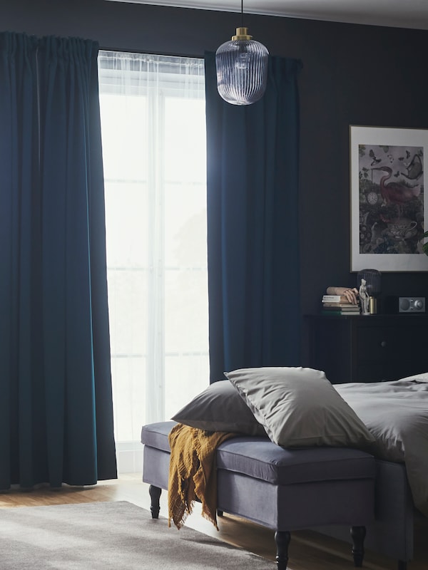 卧室与暗蓝绿色MAJGULL屏蔽窗帘和窗帘在一个大窗口对面的床和一个板凳。