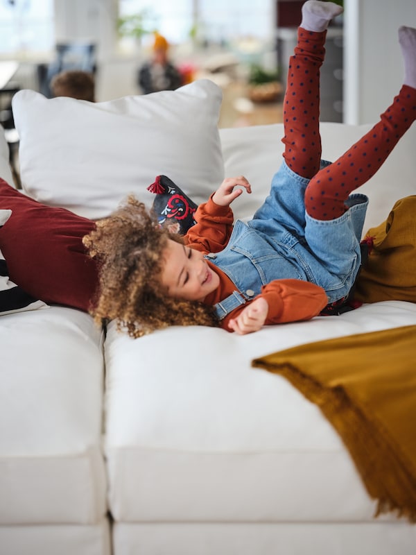 孩子快乐地滚,脚在空中,在五颜六色的纺织品在白色GRONLID阀座沙发和躺椅。