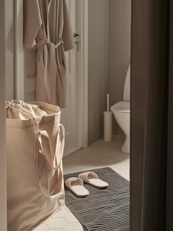 一个完整PURRPINGLA洗衣袋的浴室门上挂着浴袍,回来。一双拖鞋在地板上。