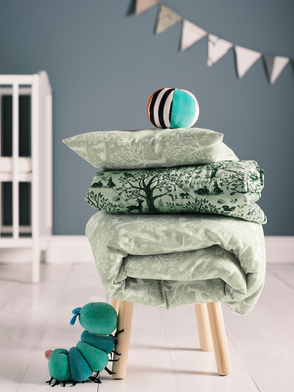 儿童粪便堆折叠羽绒被和枕头覆盖着绿色TROLLDOM床单和KLAPPA毛绒玩具球。