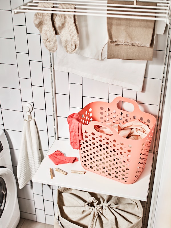 架子上的粉色SLIBB灵活的洗衣篮白色衣服结合一个晒衣架,加上一个米色洗衣袋。