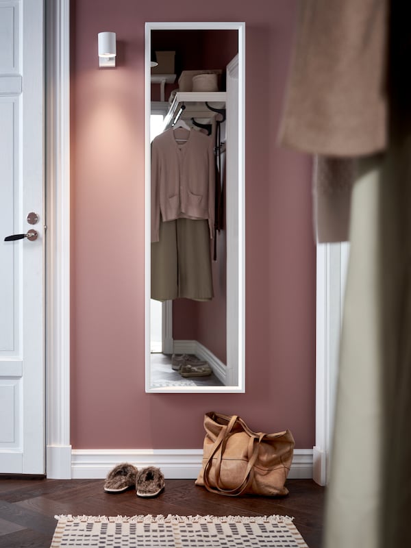 一块巨大的白色NISSEDAL镜子在走廊的墙上,一袋,一双鞋和一个多色地毯在地板上。