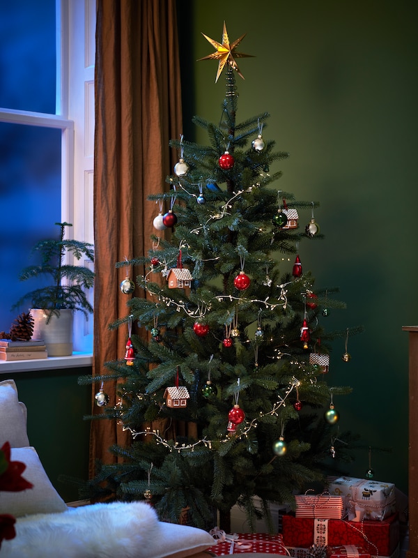 靠近窗户的圣诞树上装饰着VINTERFINT小玩意和STRÅLA LED树顶星和灯饰链。