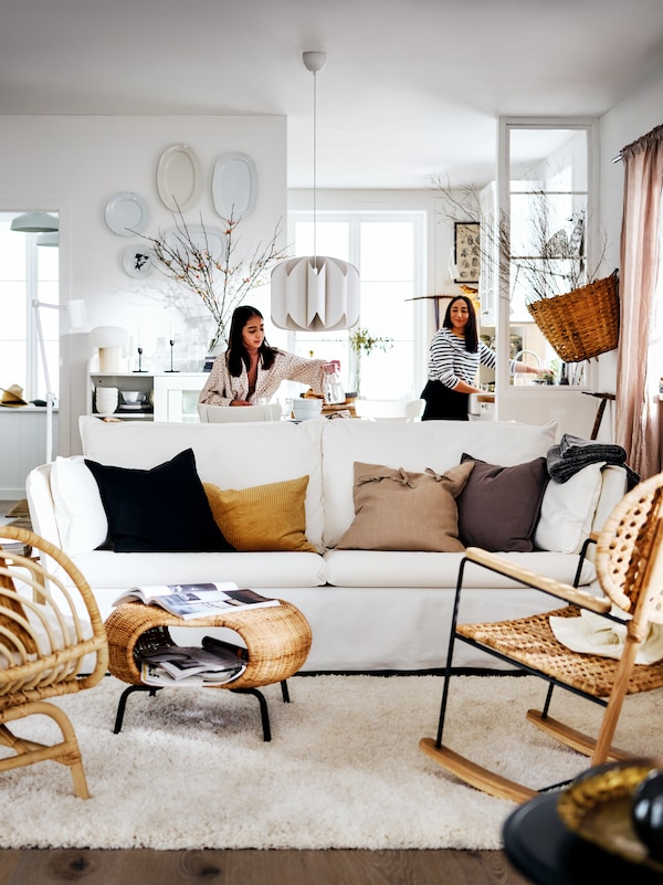 白色BACKSALEN沙发和两个扶手椅在明亮的乡村式的生活区域和两个女人在房间的后面。