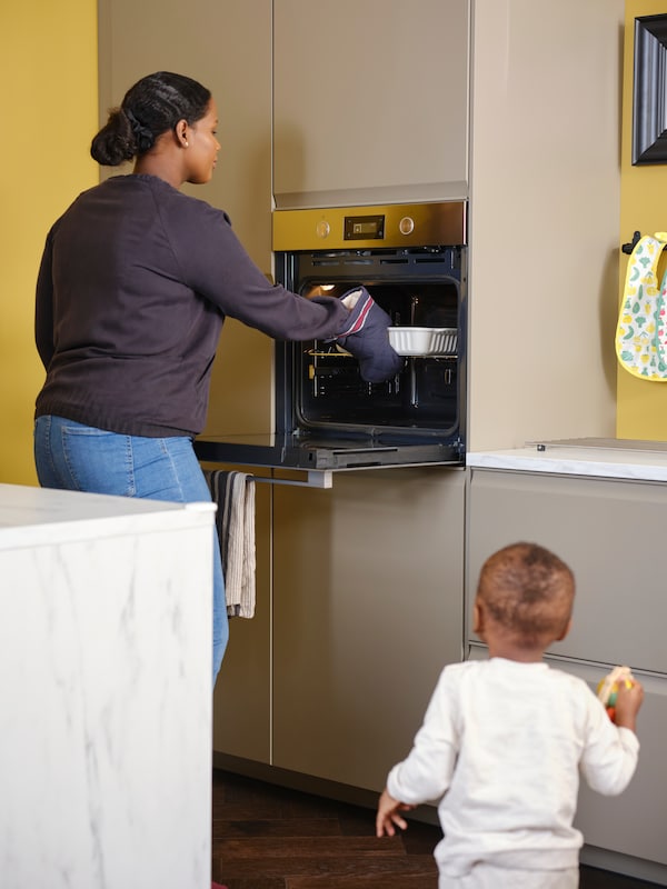 一个蹒跚学步的孩子看起来像一个女人需要烤箱菜的ANRATTA强迫通风烤箱在厨房马特黑色米色方面。