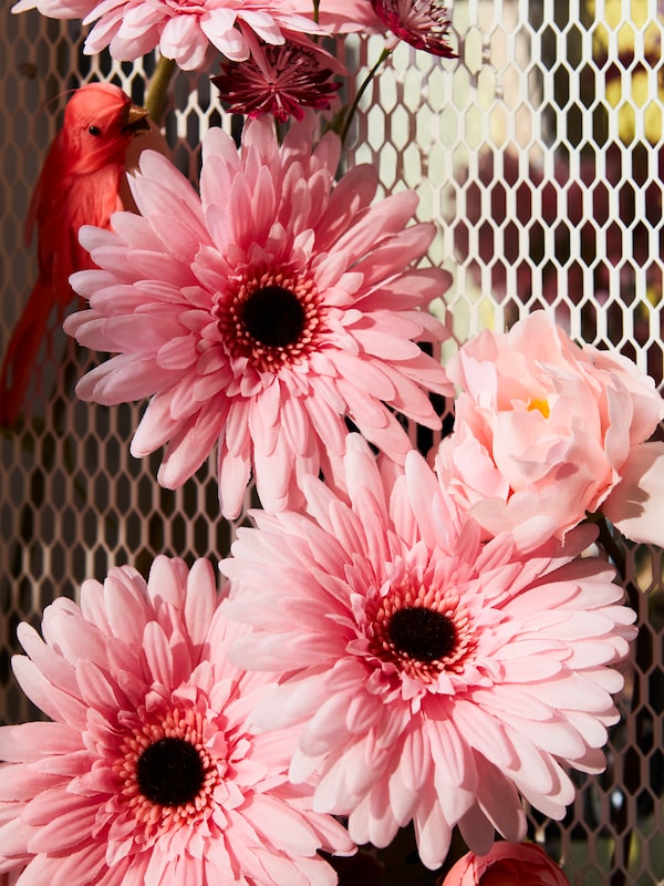 SMYCKA粉色人造花和一只装饰鸟的特写，在BAGGEBO橱柜的网格侧板内。