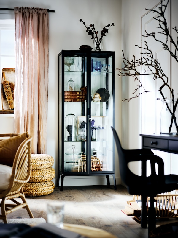 黑色MILSBO内阁玻璃门,里面填满了各式各样的对象,一个明亮的客厅的角落里。