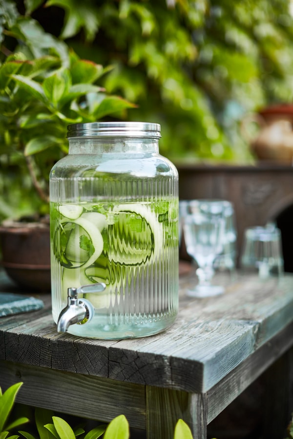 VARDAGEN jar自来水含有水和条黄瓜站在边缘的一个表在一个平台。