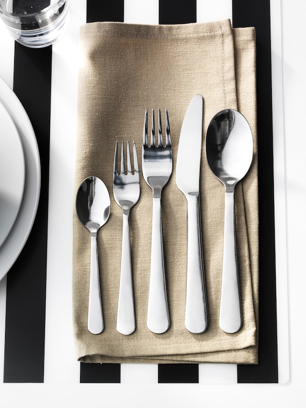 黑白条纹的地方垫用餐巾拿着一把刀,两个叉子和两个勺子从龙餐具。