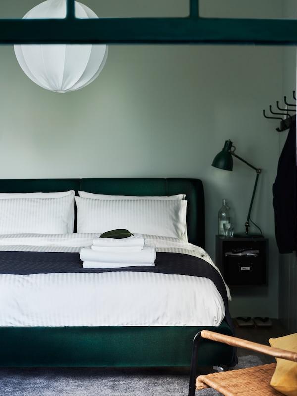 一个卧室TUFJORD深绿色软垫床框架与黑和白色的床单扔交叉在最后。