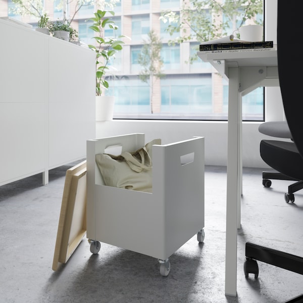 白色与顶部装有轮子TROTTEN存储单元和一个米色袋里面,一张桌子和一个办公室旁边的椅子上。