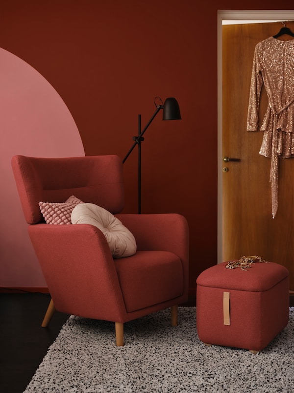 核废料翼椅子和脚凳Tonerud红色坐在一个房间里,红色的墙和衣服挂在门上。