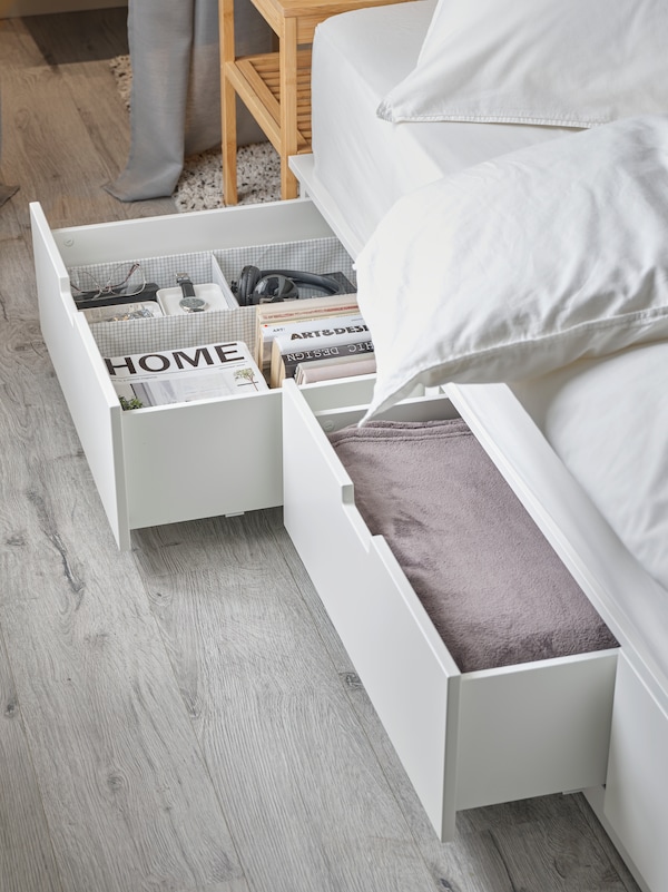 白色的床下面NORDLI帧存储。两个抽屉的开放和包含书籍,一个床罩和各种物品。