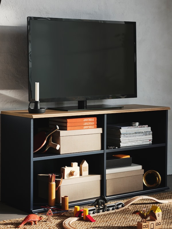 黑色电视是穿着蓝黑色的SKRUVBY电视上盒,书,玩具和乒乓球球拍的货架上。