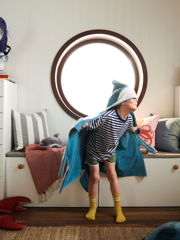一个男孩,裹着BLAVINGAD棉毛巾罩,假装鲨鱼在一个圆形窗口的前面。