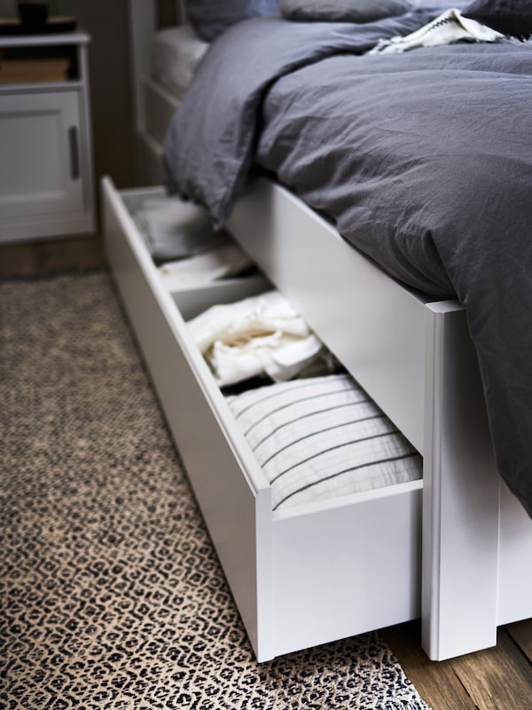 白色SONGESAND床2存储盒,打开显示折叠纺织品。灰色ANGSLILJA床单在床上。