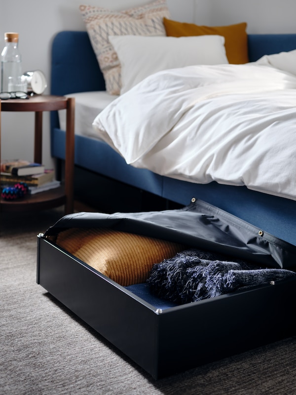 黑色的床与缓冲存储箱和床罩,旁边一个软垫床床头板框架角落。