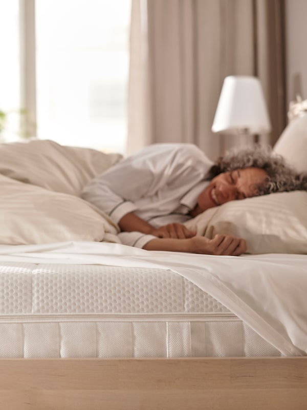 女人在睡衣躺在桦树床白色AKREHAMN泡沫床垫用白色条纹床单。