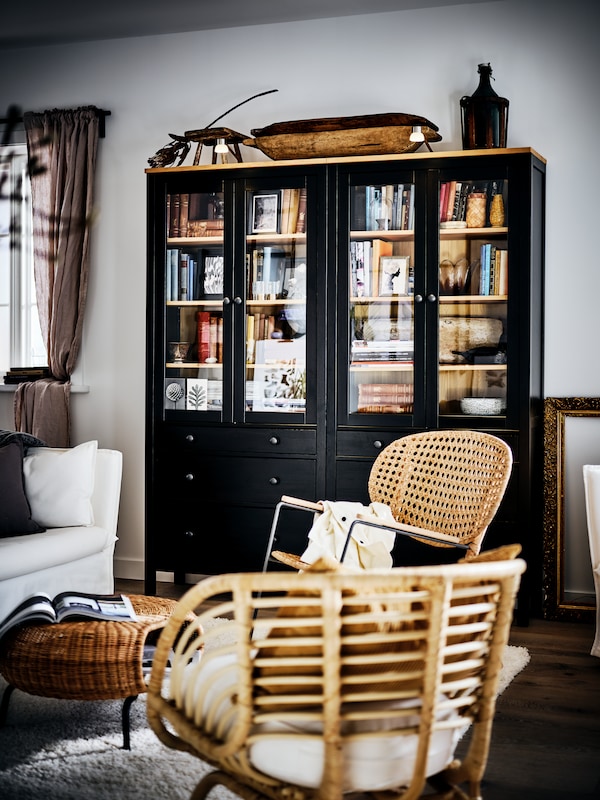 两个黑HEMNES玻璃门橱柜塞满了书,乡村式的客厅,两把椅子和一个沙发。