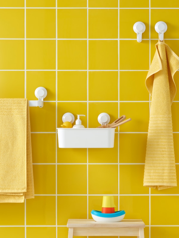 TISKEN håndklestang med sugekopp og TISKEN kurv med sugekopp, begge i hvitt, i et bad med gule fliser。