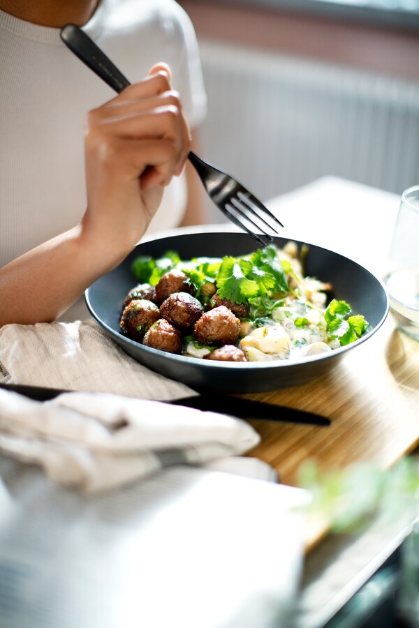 一只手拿着叉子上面一盘HUVUDROLL植物球和绿色蔬菜在木桌旁边一些茶巾。