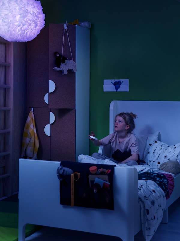 一个女孩使用STYRBAR遥控TRADFRI LED灯泡的颜色改为蓝色VINDKAST吊灯。