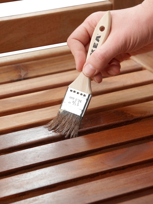 一只手拿着画笔,画窄木条在一张户外家具和污渍。