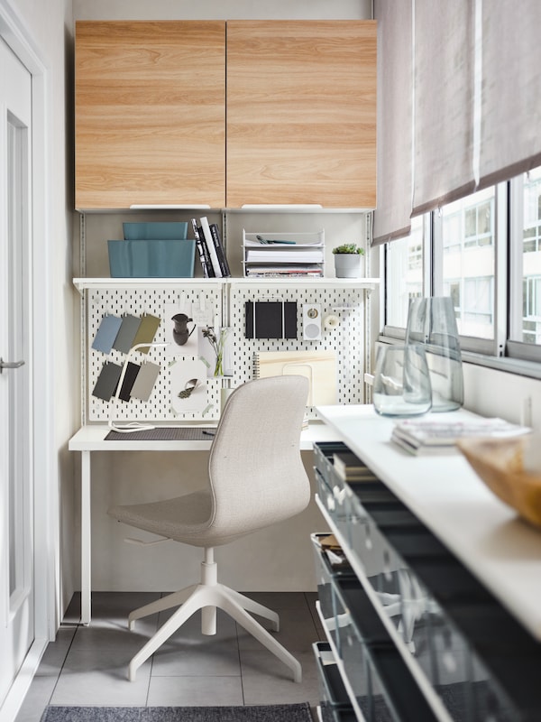 En kontorstol, et hvidt skriveboard, hvide opslagstavler, et BOAXEL opbevaringssystem og hylder samt ENHET skabe i hvid/eg。