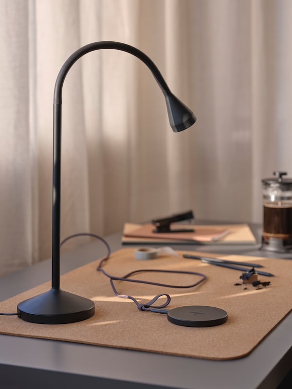 黑色NAVLINGE LED工作灯站在软木SUSIG办公桌垫在桌子附近的一个黑色LIVBOJ无线充电器。