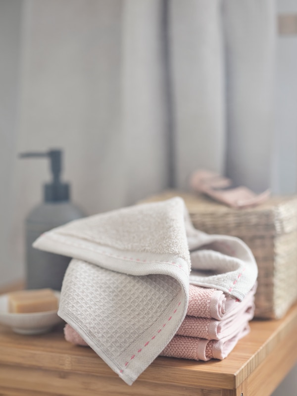 棉花VARDANDE毛巾用手缝缝合折叠在一堆粉红色毛巾浴室木制柜台上。